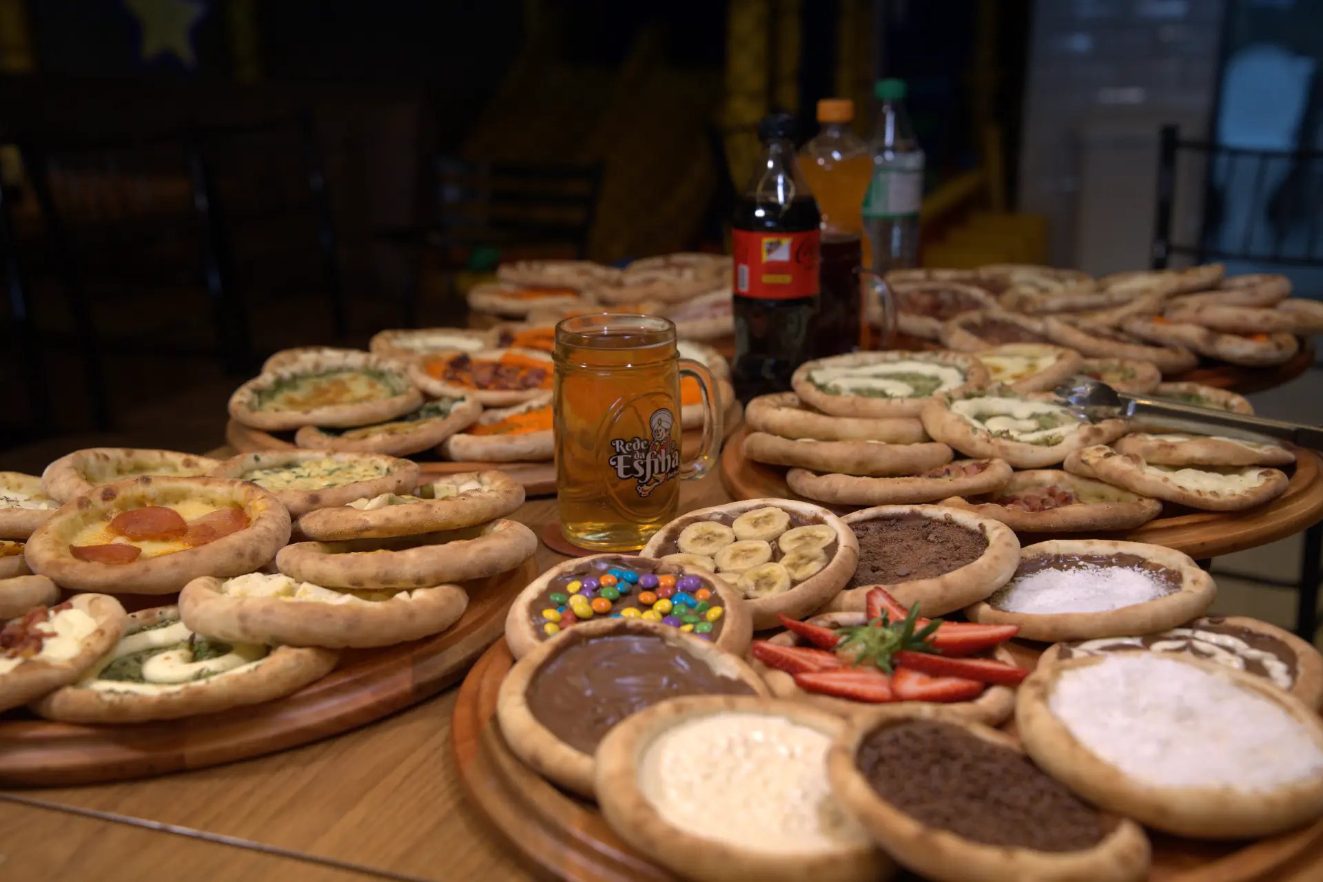 Mesa com variedade de esfihas salgadas e doces e caneca da Rede Da Esfiha